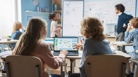 Deux étudiants dans une salle de classe consultent ensemble un organigramme sur le même ordinateur portable.