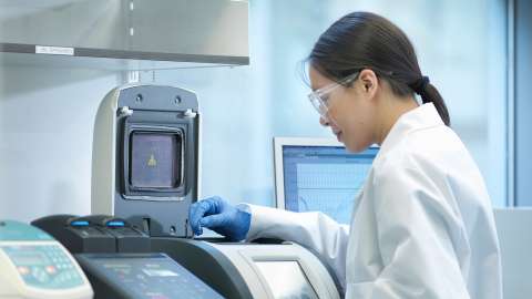 Un technicien de laboratoire se tient devant une machine d'analyse d'échantillons pour surveiller la progression